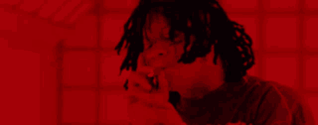a man with dreadlocks is smoking a cigarette in a dark room with a red light behind him .