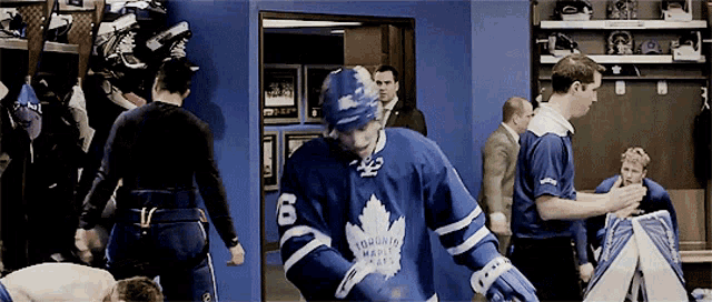 a hockey player in a toronto maple leafs jersey stands in a locker room
