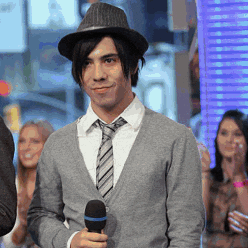 a young man wearing a hat and tie holds a microphone