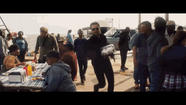 a group of people are gathered around a picnic table including a man carrying a box