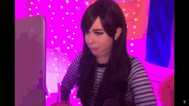 a woman in a wig is sitting in front of a laptop computer in a pink room .