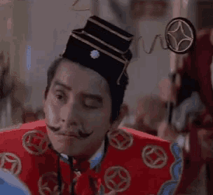 a man with a mustache and a hat is wearing a red robe and a black hat .