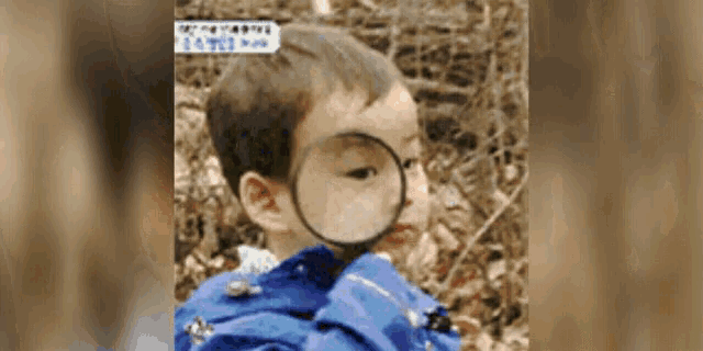 a young boy is looking through a magnifying glass at something .