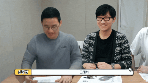 a man wearing glasses sits at a table with a yellow speech bubble that says ' 신 '