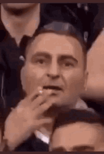a man is sitting in a crowd of people with his hand on his mouth .