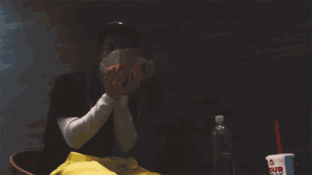 a man holds a bunch of money in front of a cup that says our