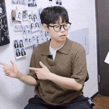 a young man wearing glasses and a brown sweater is pointing at something