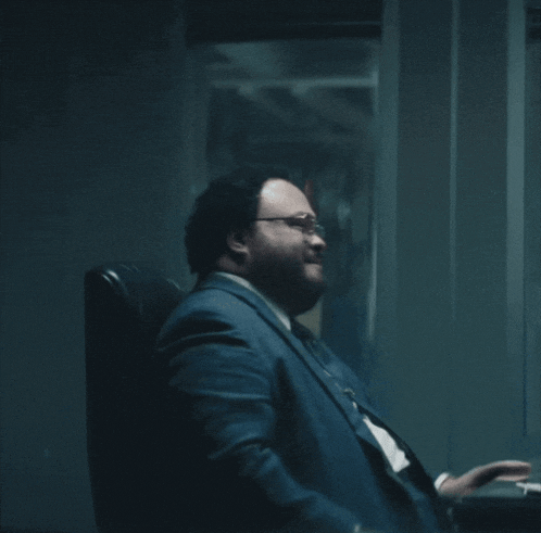 a man in a suit and tie is sitting in a chair with the words that 's hot above him