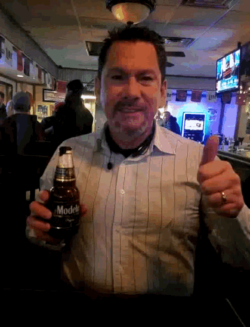 a man giving a thumbs up while holding a bottle of modelo beer