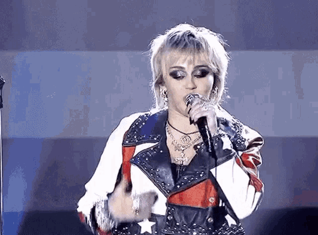 a woman is singing into a microphone while wearing a leather jacket .