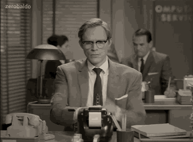 a man in a suit and tie is sitting at a desk in front of a sign that says computer service