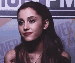 ariana grande is wearing red lipstick and a necklace while standing in front of a sign .
