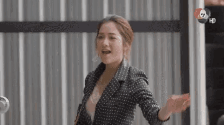 a woman in a black and white polka dot jacket is standing in front of a wall with her arms outstretched .