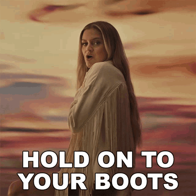 a woman in a fringed jacket stands in front of a sunset and says " hold on to your boots "