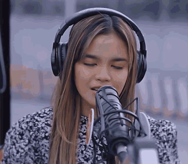 a woman wearing headphones singing into a microphone with her eyes closed
