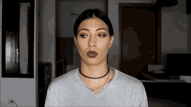 a woman wearing a choker and a grey shirt is making a funny face