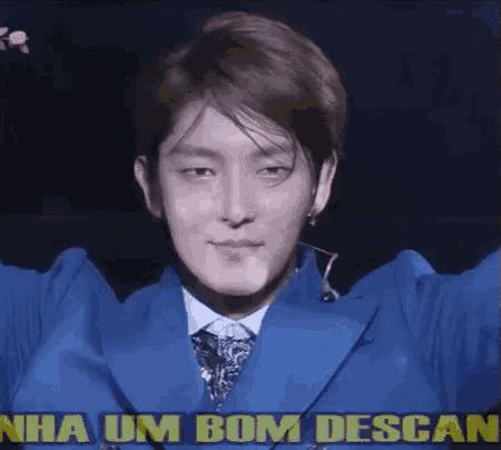 a man in a blue suit and tie is standing in front of a sign that says nha um bom descans .