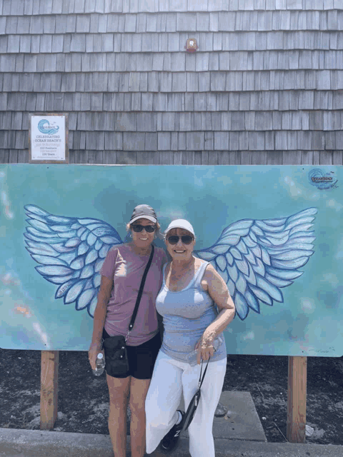 two women standing in front of a painting of wings