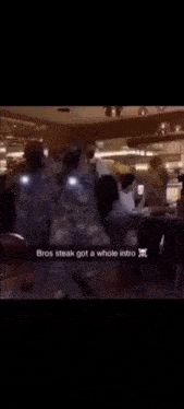 a man in a white shirt is standing in front of a group of people and says " bros steak got a whole intro " .