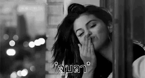 a black and white photo of a woman blowing a kiss while looking out a window .