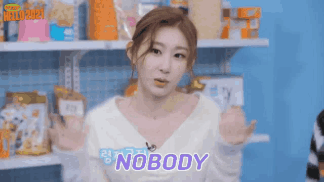 a woman in a white sweater is standing in front of a shelf and says nobody .