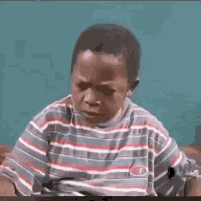 a young boy wearing a striped shirt is sitting on a couch making a funny face .