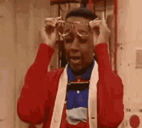 a man wearing a red sweater and a blue shirt is putting on glasses .