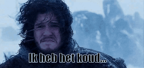 a man with long hair and a beard is standing in the snow with the words ik heb het koud written above him .