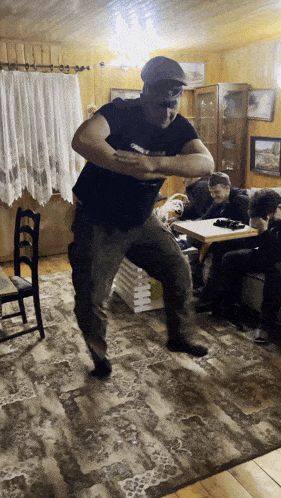 a man is dancing in a living room with a man sitting on a couch in the background
