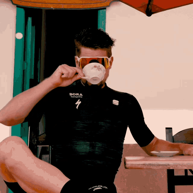 a man wearing sunglasses and a shirt that says bora is drinking from a cup