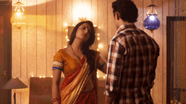 a man in a plaid shirt stands next to a woman in a red sari
