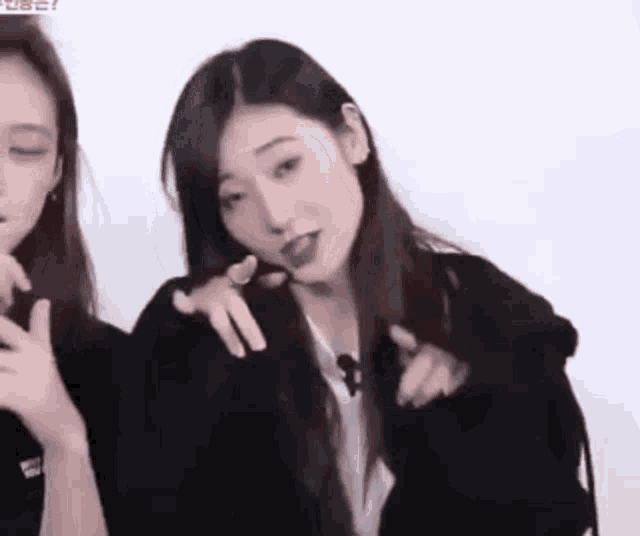 a couple of girls are standing next to each other and one of them is pointing at the camera .