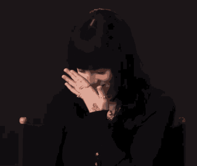 a woman with black hair and a tattoo on her arm is covering her mouth with her hands .