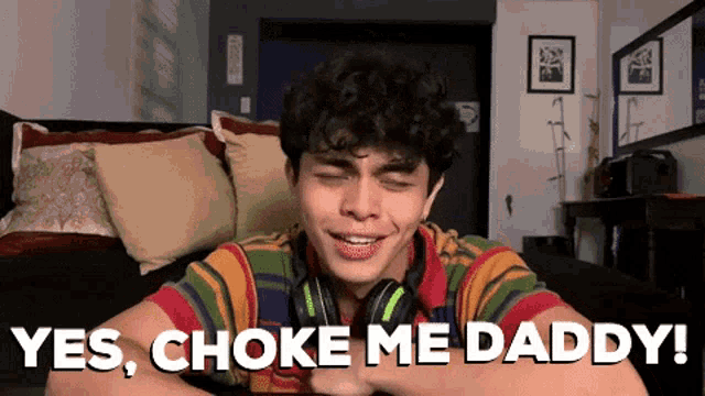 a young man wearing headphones is sitting on a couch and says yes choke me daddy