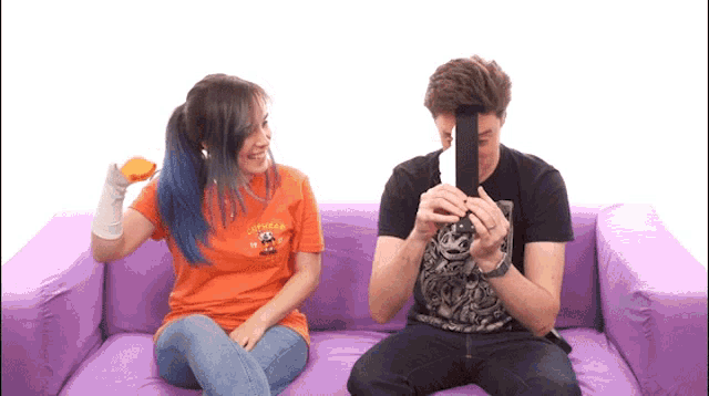a man and a woman are sitting on a purple couch and the woman is wearing an orange shirt that says lifeguards on it