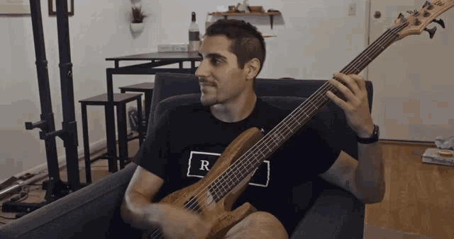 a man in a black shirt with the letter r on it holds a guitar