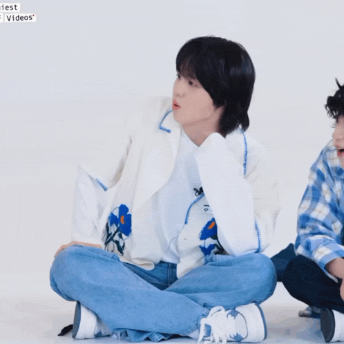 a man in a white jacket sits on the floor next to a man in a plaid shirt