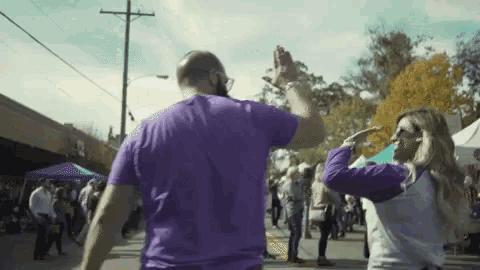 a man and a woman are giving each other a high five while dancing on a street .