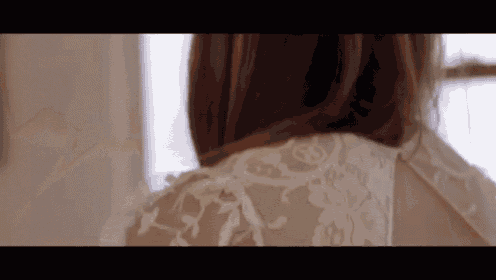 a woman in a white lace dress is looking at herself in the mirror .