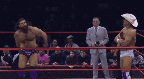 a man in a cowboy hat is standing in a wrestling ring with two other men