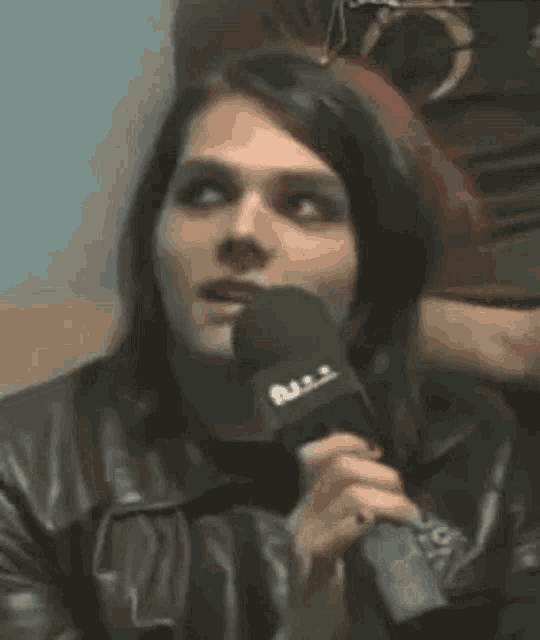 a man in a leather jacket is holding a microphone in front of his mouth .
