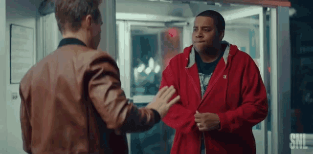 a man in a red jacket is talking to another man .