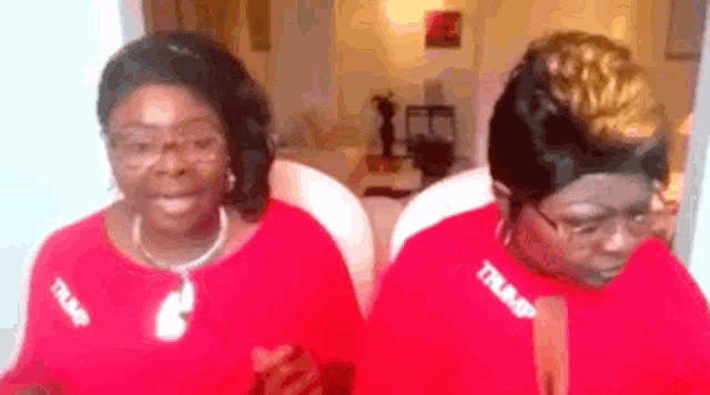 two women wearing red shirts that say trump are sitting next to each other in a living room .