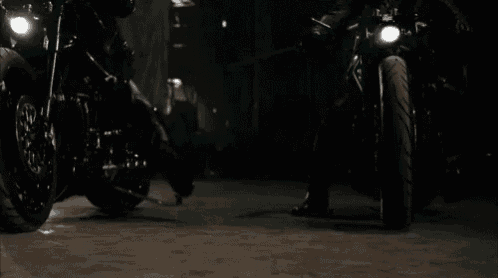 two people are riding motorcycles in the dark with their lights on .