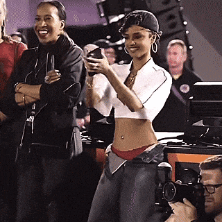 a woman in a crop top is taking a picture of herself in front of a crowd .
