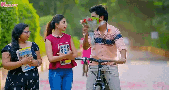 a man is holding a bouquet of flowers in front of his face while two women look on .