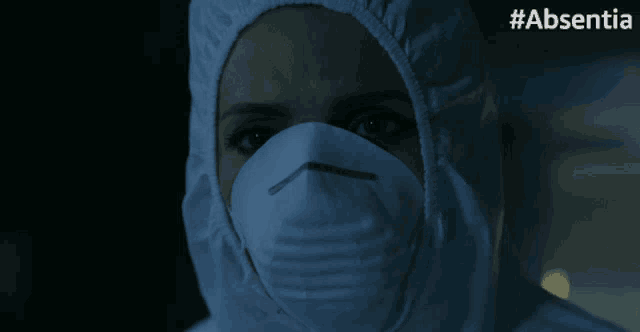 a close up of a person wearing a protective suit and mask with #absentia written on the bottom