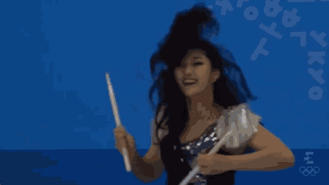 a woman is holding a drum stick in front of a blue background with tokyo written on it