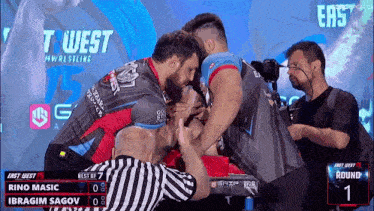 rino masic and ibragim sagov arm wrestling in front of a screen that says east west