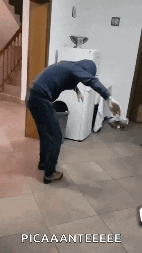a man in a hooded jacket is standing in front of a refrigerator and a trash can ..